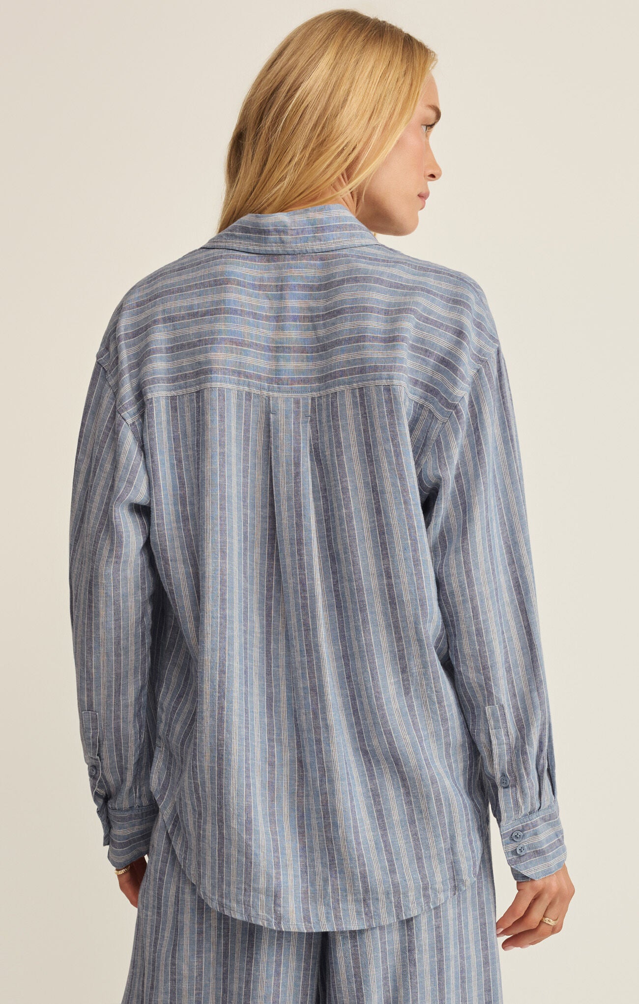 Person wearing a blue striped shirt and pants on a beige background