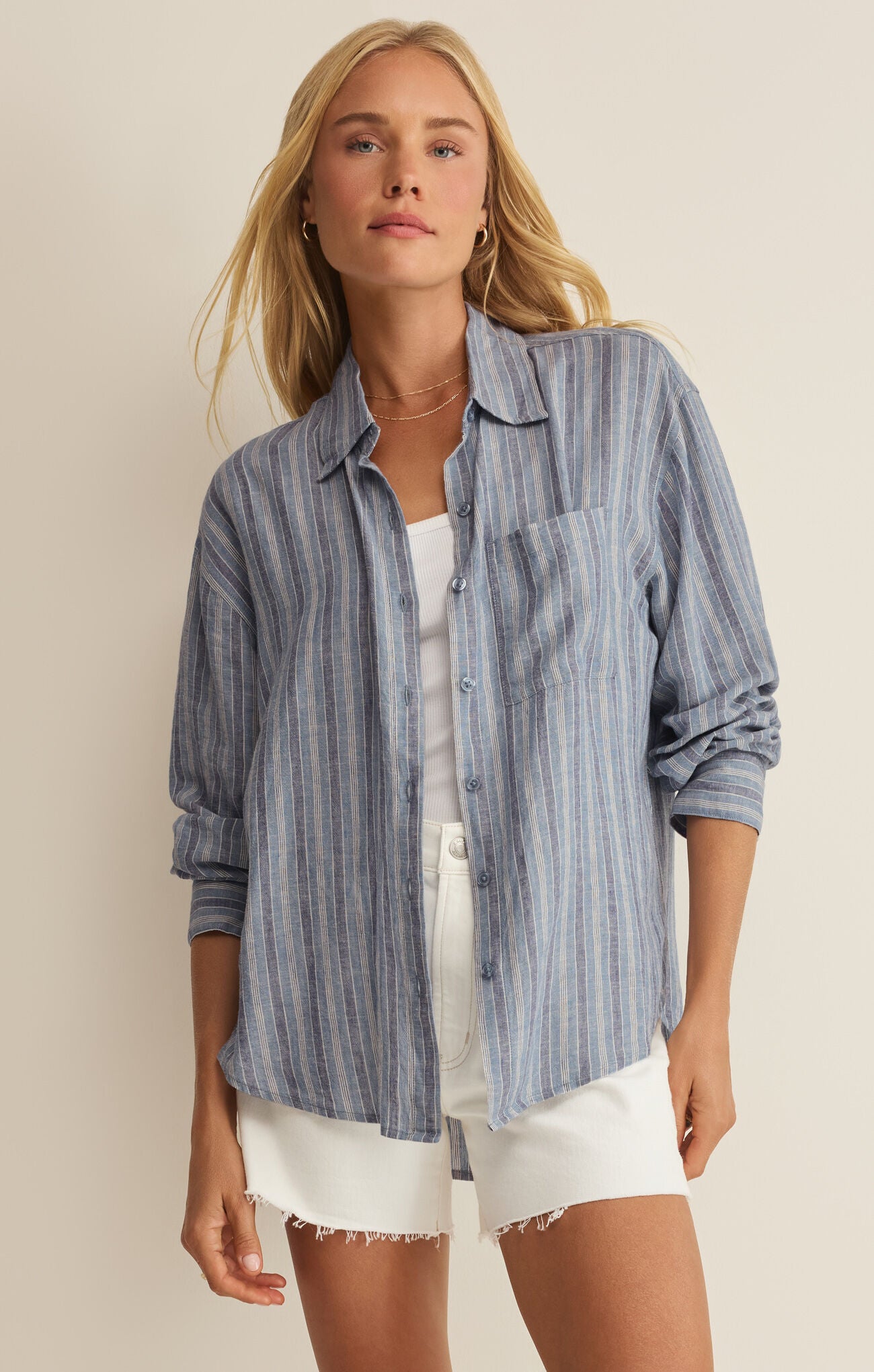 Woman wearing a blue striped shirt and white shorts on a beige background
