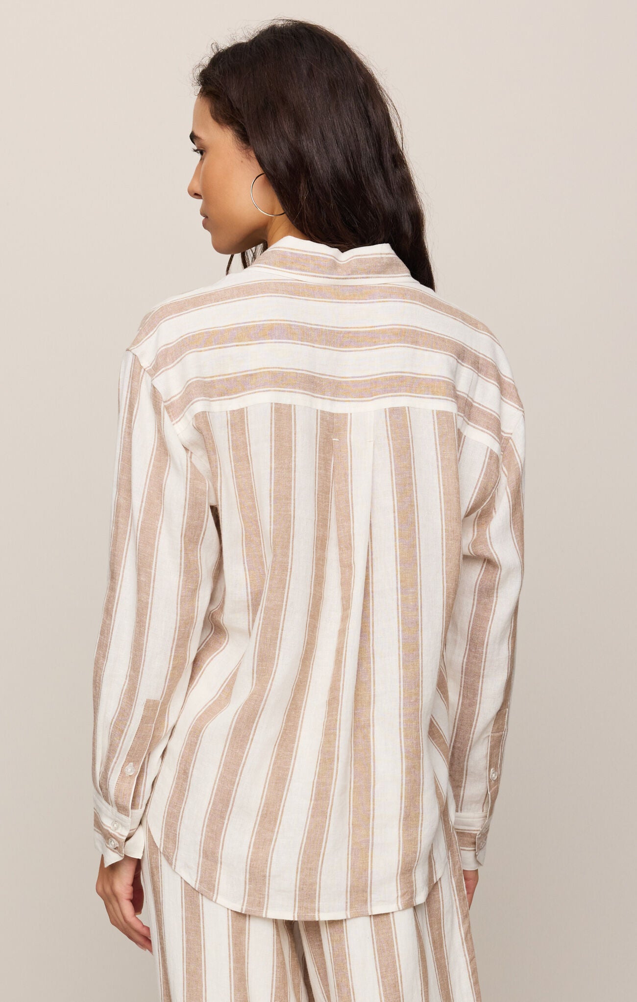 Woman wearing a beige and white striped shirt against a beige background
