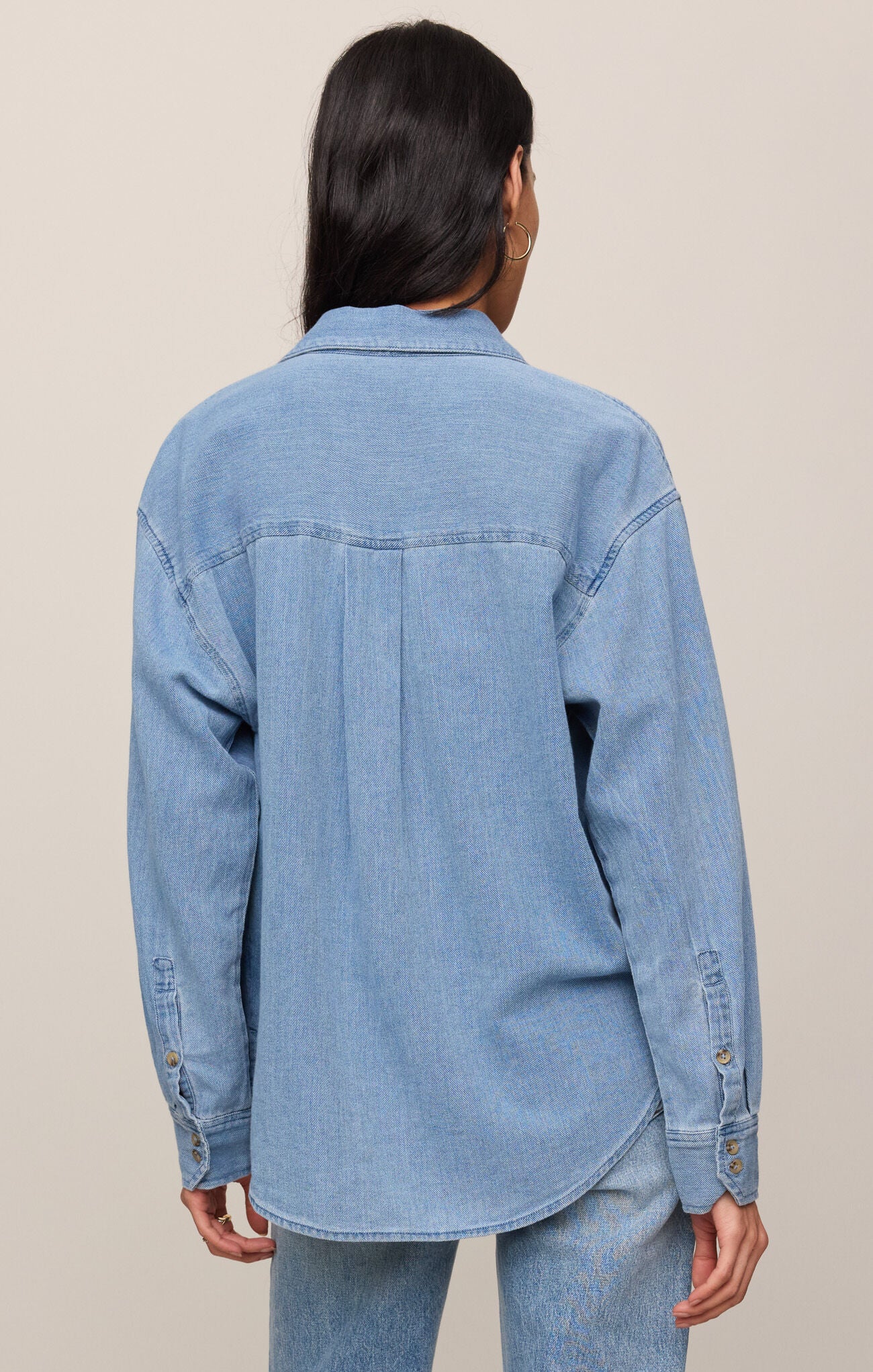Person wearing a light blue denim jacket on a beige background