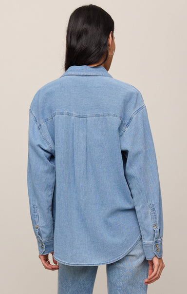 Person wearing a light blue denim jacket on a beige background