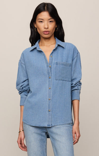 Woman wearing a light blue denim shirt and jeans on a beige background