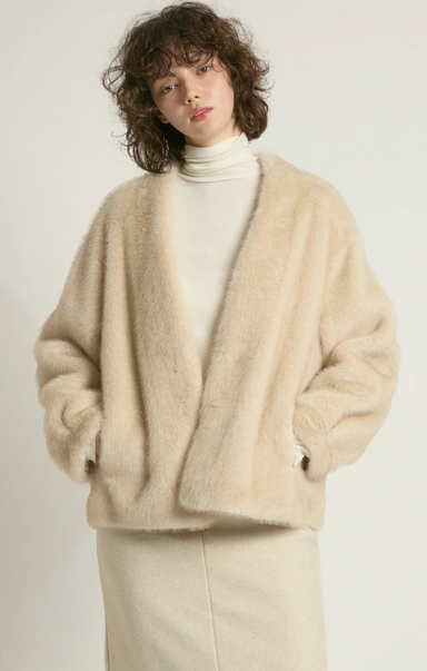 Person wearing a beige cardigan over a white turtleneck on a plain background