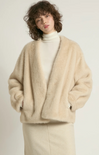 Person wearing a beige cardigan over a white turtleneck on a plain background