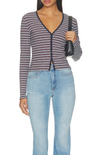 A woman wearing a long-sleeve striped cardigan with a V-neck and front zipper, paired with light-wash blue jeans, holding a black shoulder bag against a plain white background.