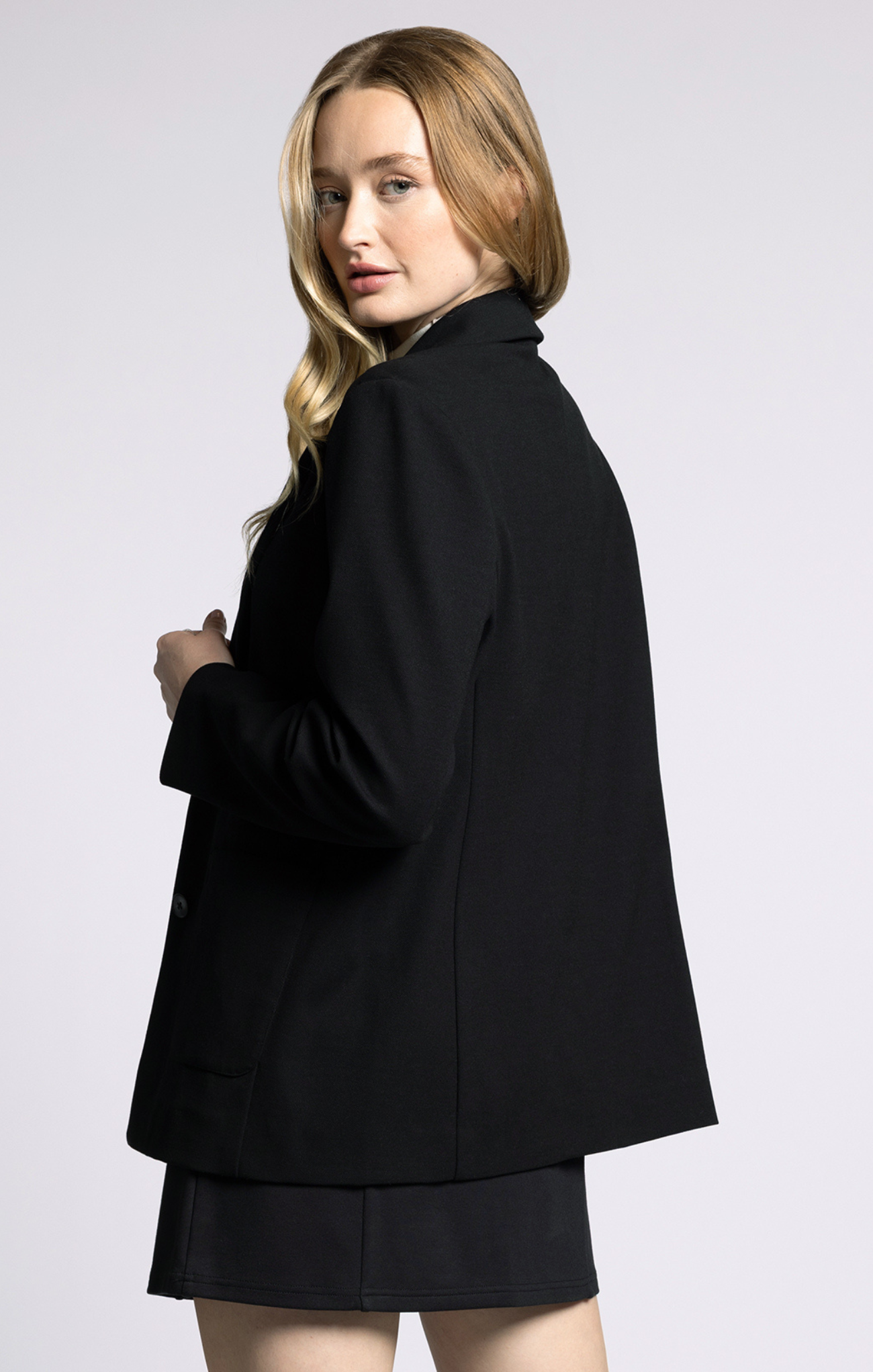 Woman wearing a black blazer and skirt set on a light gray background