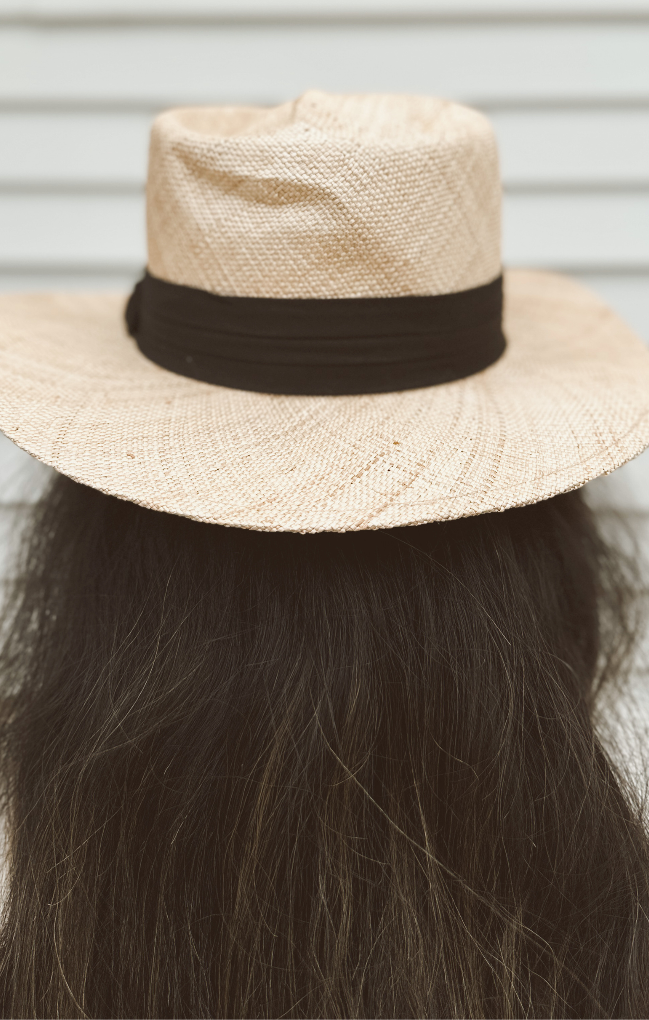 Beige straw hat with a brown band on a mannequin head against a neutral background