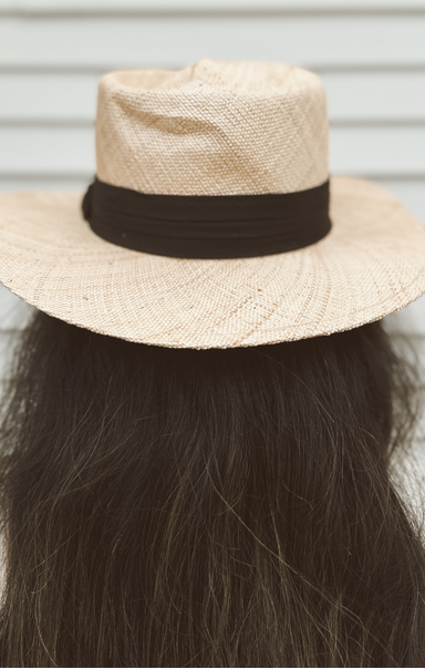 Beige straw hat with a brown band on a mannequin head against a neutral background