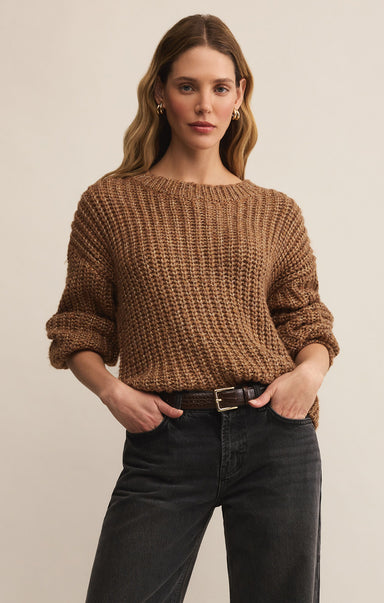 Woman wearing a brown knitted sweater and black jeans against a beige background