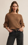 Woman wearing a brown knitted sweater and black jeans against a beige background