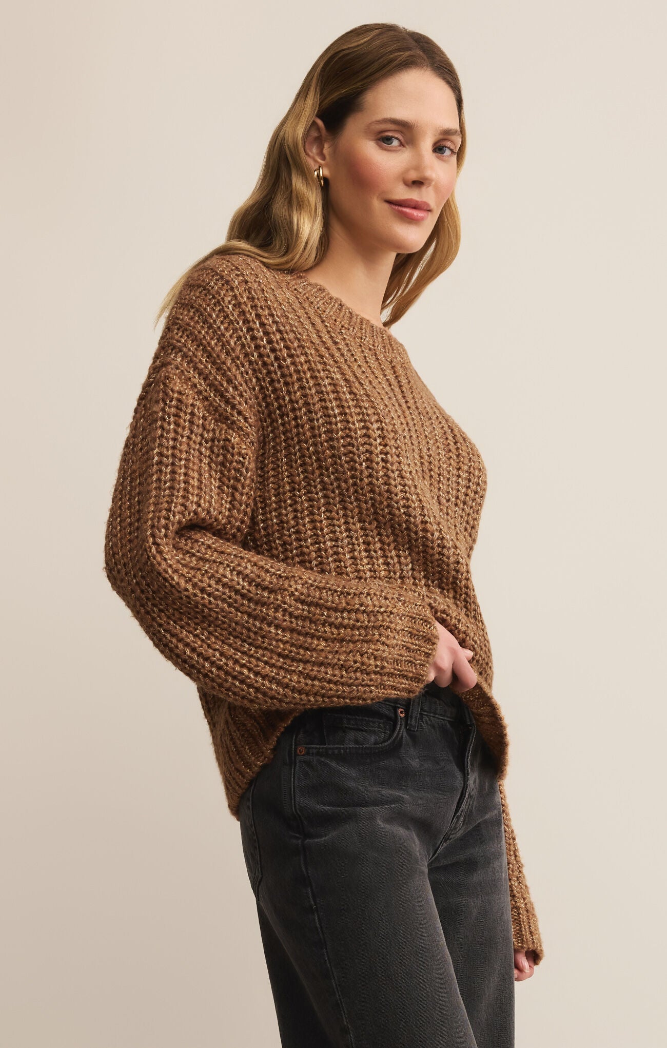 Woman wearing a brown chunky knit sweater against a plain background