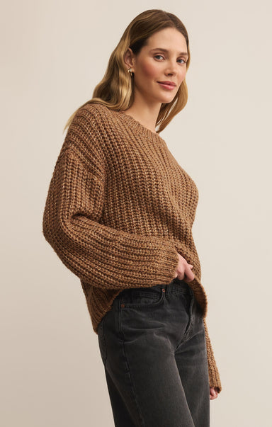 Woman wearing a brown chunky knit sweater against a plain background