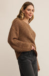 Woman wearing a brown chunky knit sweater against a plain background