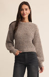 Woman wearing a textured sweater and dark jeans against a beige background