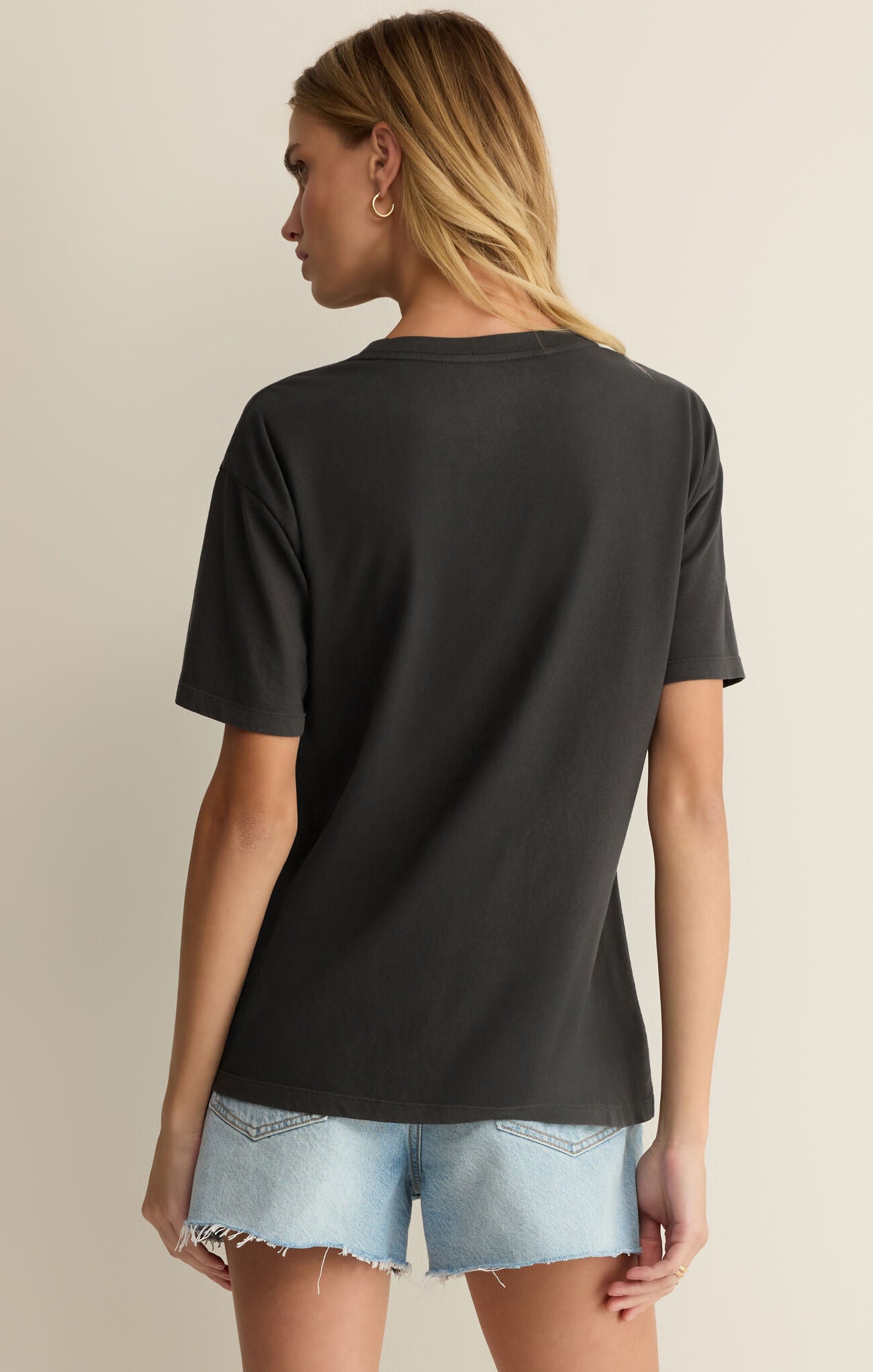 Woman wearing a black t-shirt and denim shorts on a beige background