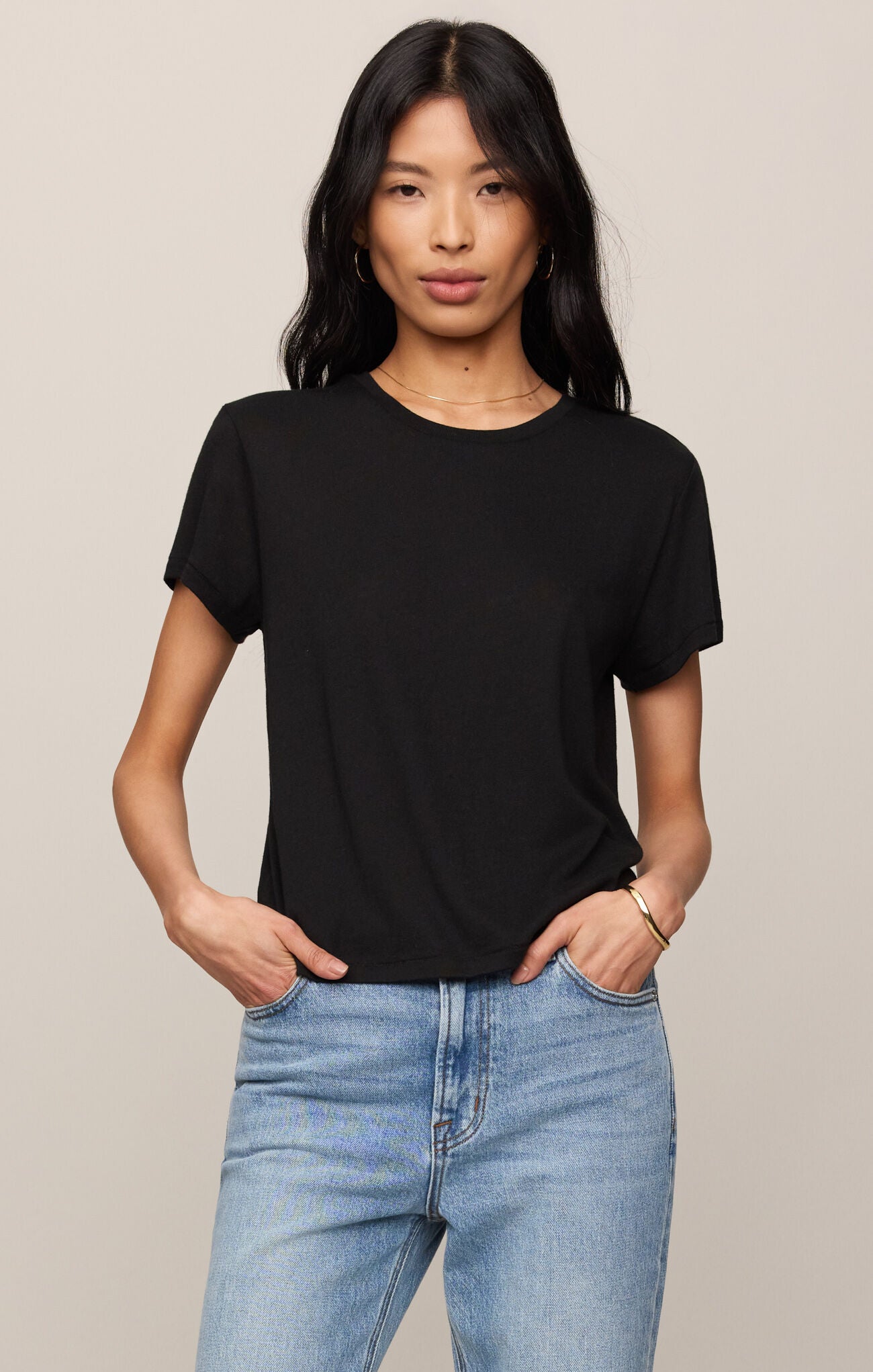 Woman wearing a black t-shirt and blue jeans against a beige background