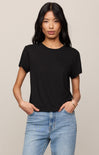 Woman wearing a black t-shirt and blue jeans against a beige background