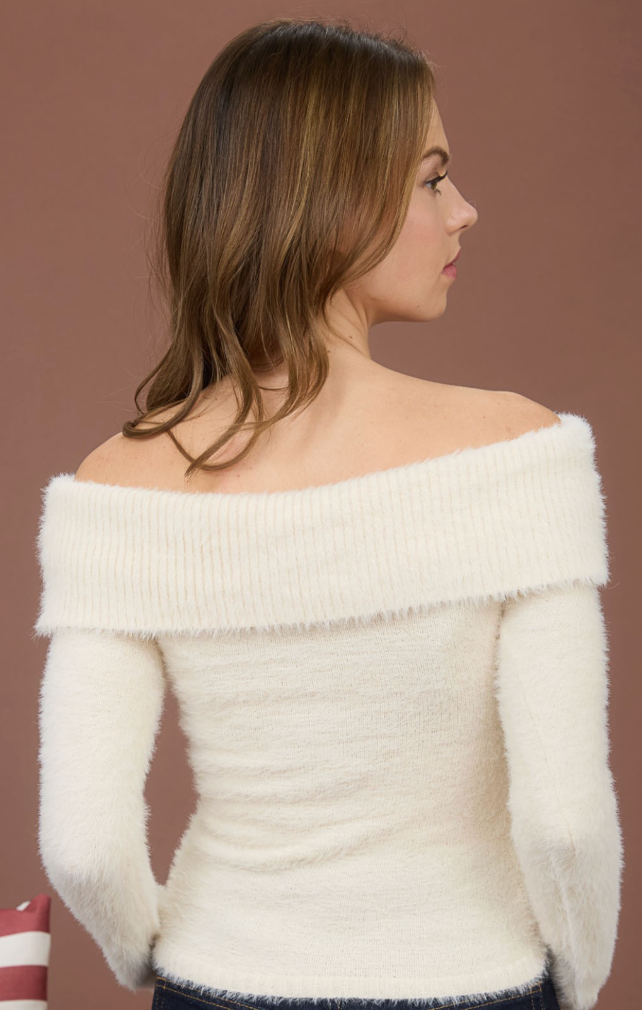 Woman wearing a white off-shoulder sweater against a brown background