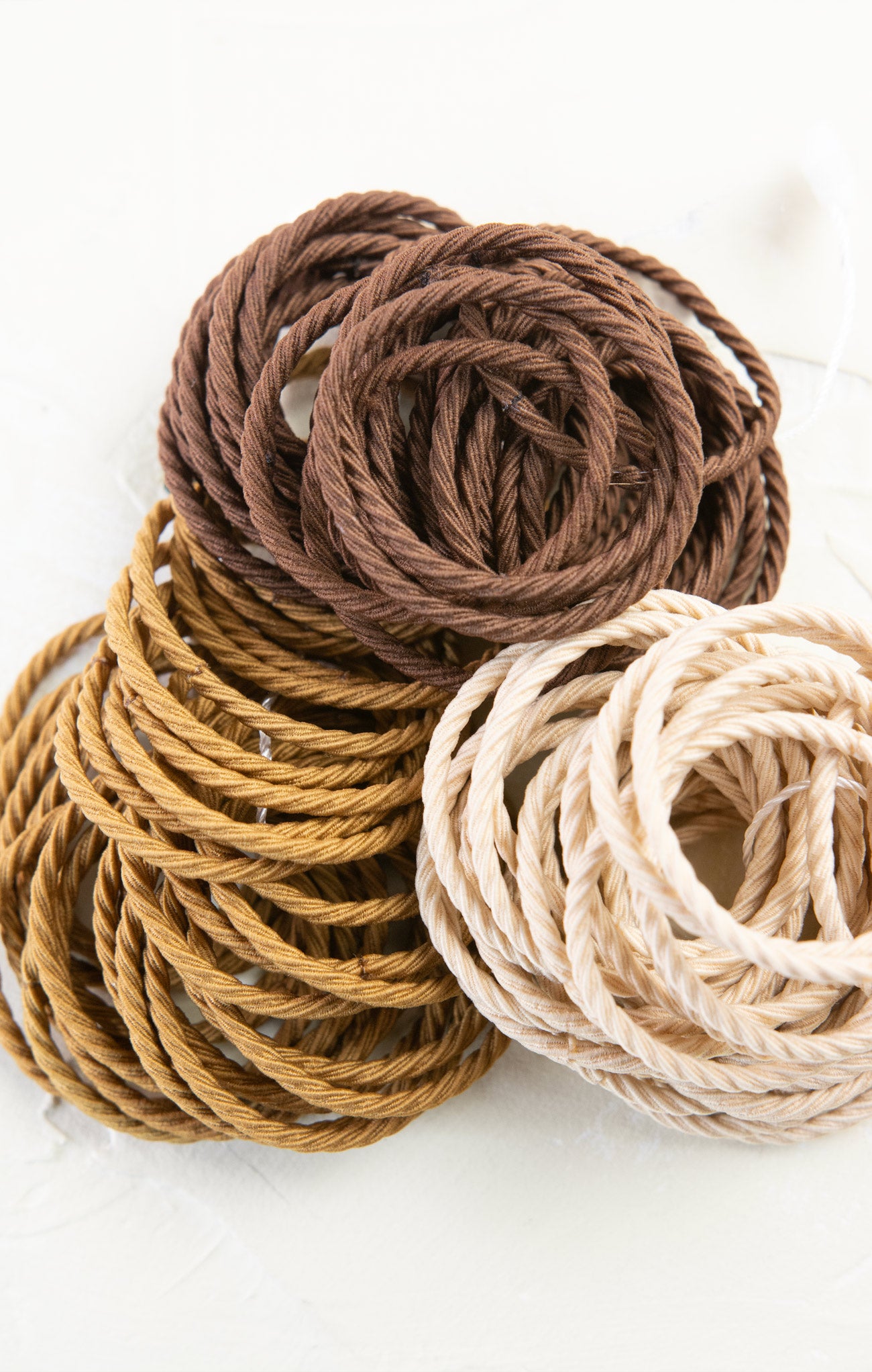 Three coiled ropes in brown, beige, and light brown on a white background