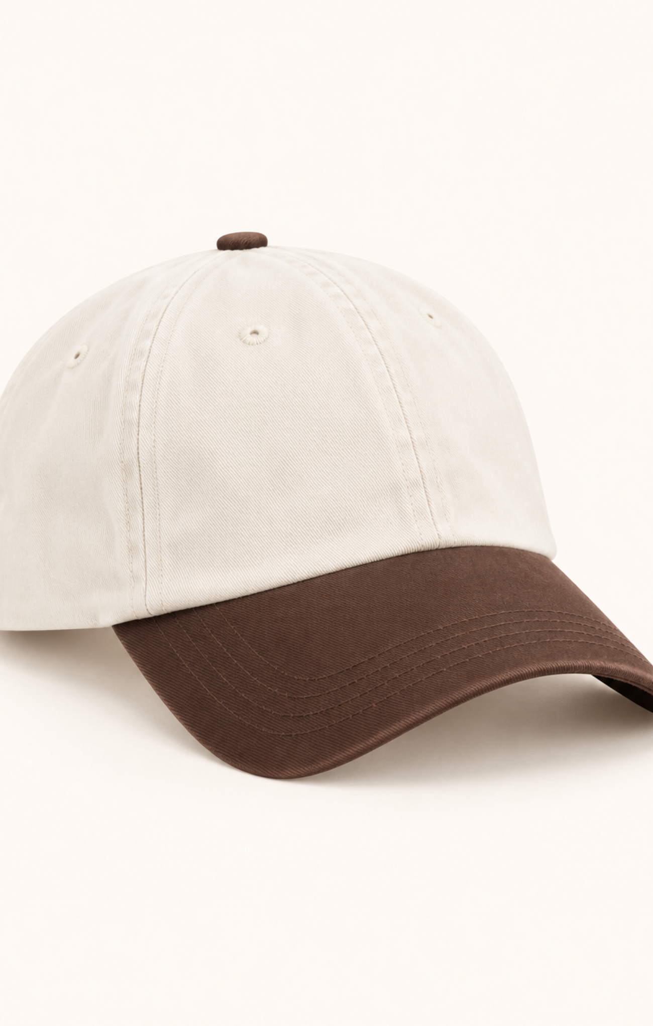 A two-tone baseball cap with an off-white crown and a dark brown curved brim, shown on a clean off-white background.
