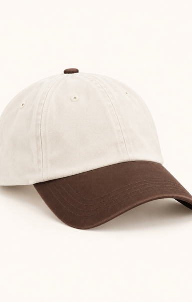 A two-tone baseball cap with an off-white crown and a dark brown curved brim, shown on a clean off-white background.