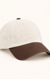 A two-tone baseball cap with an off-white crown and a dark brown curved brim, shown on a clean off-white background.