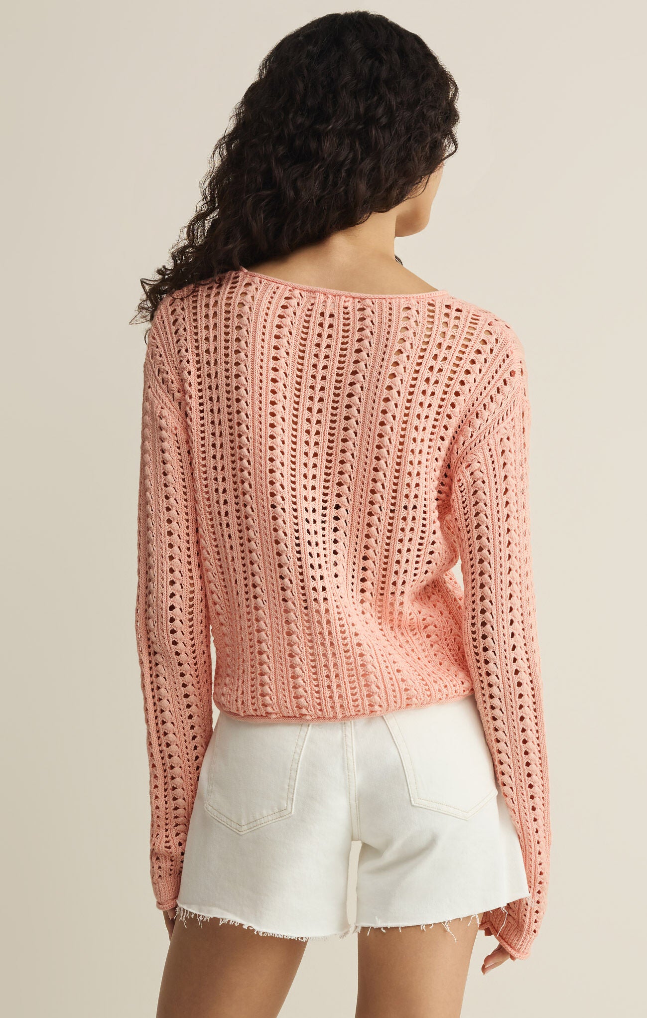 Person wearing a pink crochet sweater and white shorts on a beige background