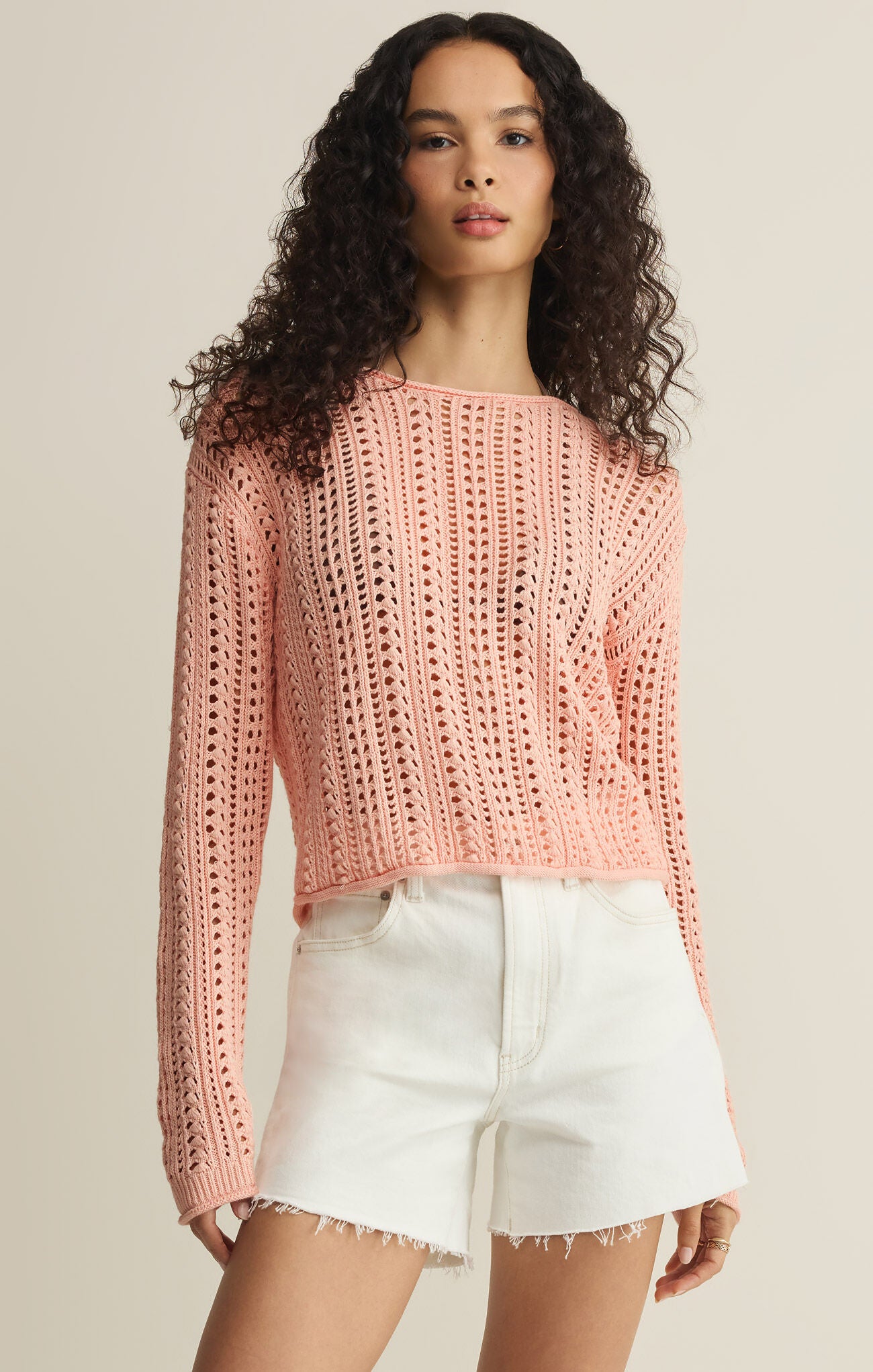 Woman wearing a pink crochet sweater and white shorts on a beige background