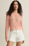 Woman wearing a pink crochet sweater and white shorts on a beige background