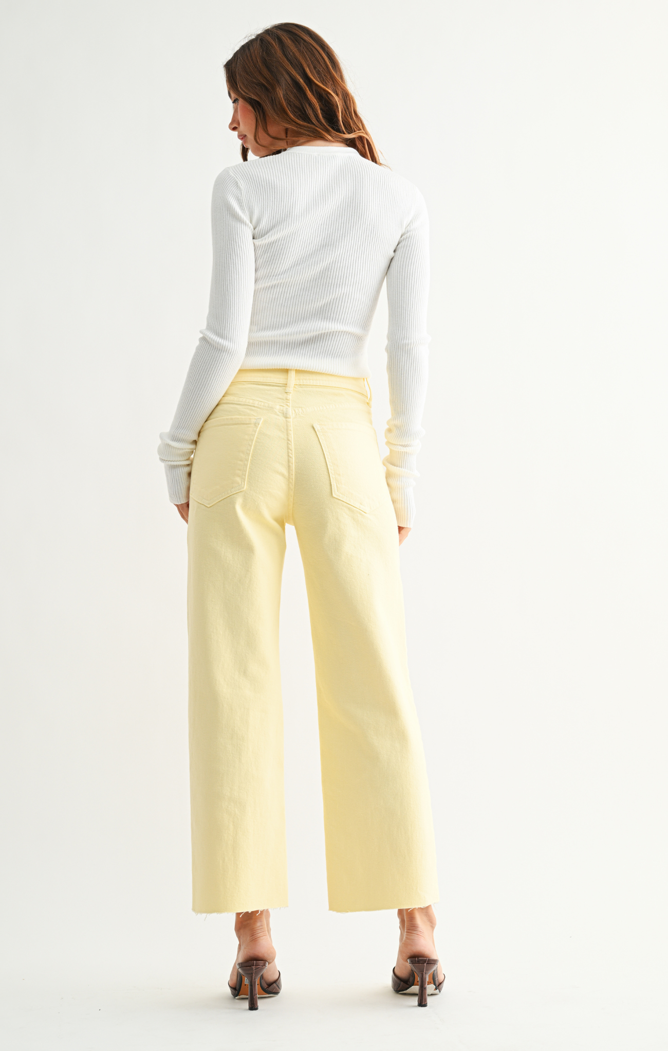 Woman wearing a white long-sleeve top and light yellow pants on a white background