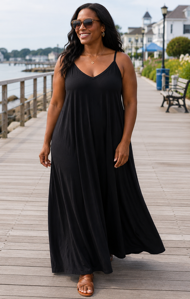 Woman wearing a black dress standing on a wooden boardwalk by a waterfront.
