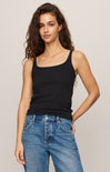 Woman wearing a black tank top and blue jeans against a plain background
