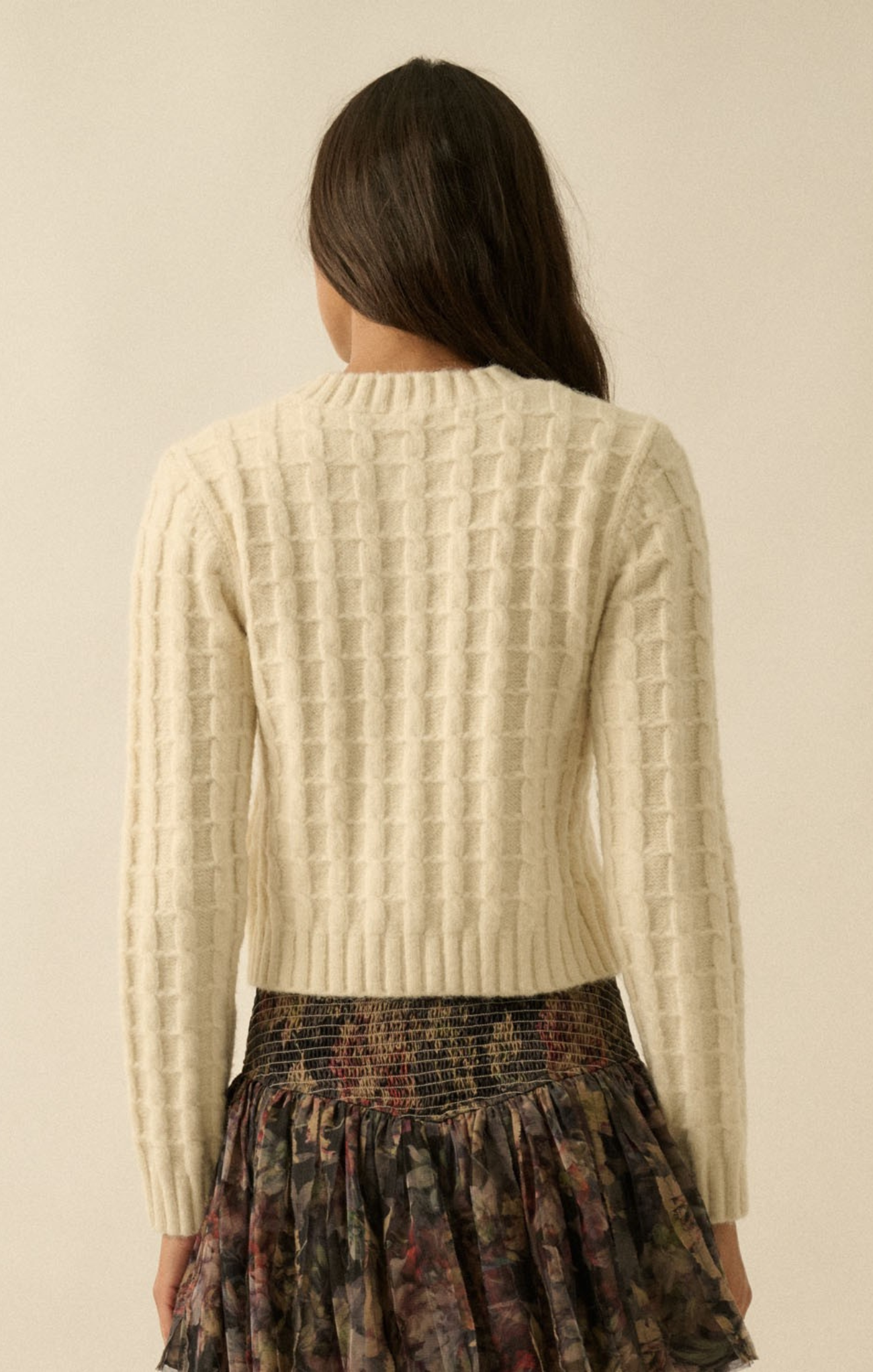 Woman wearing a beige textured sweater with a neutral background