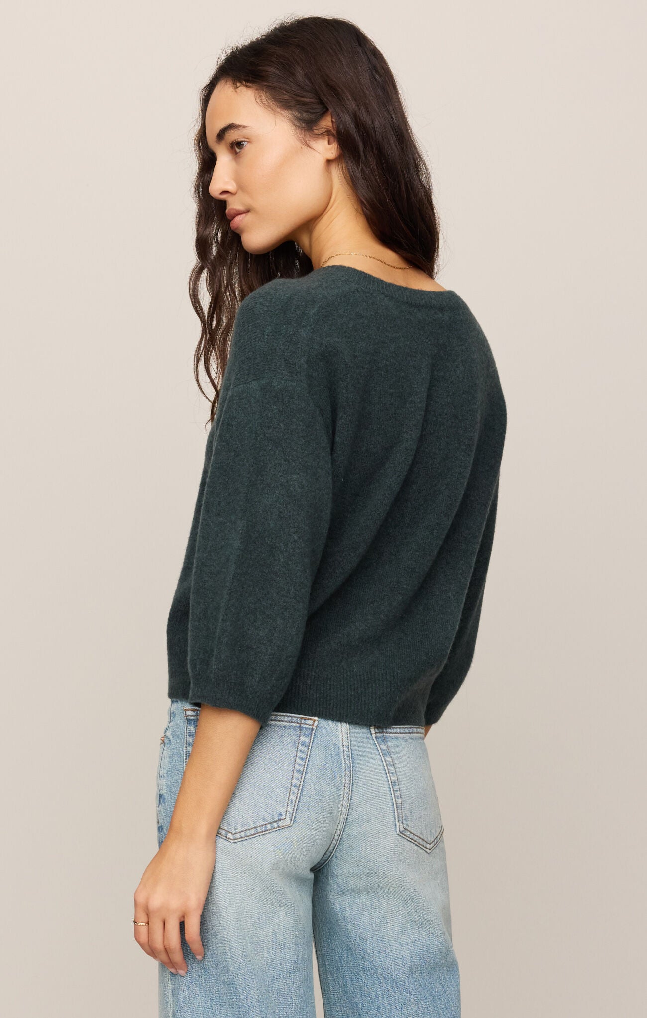 Woman wearing a dark green sweater and light blue jeans against a beige background