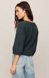 Woman wearing a dark green sweater and light blue jeans against a beige background