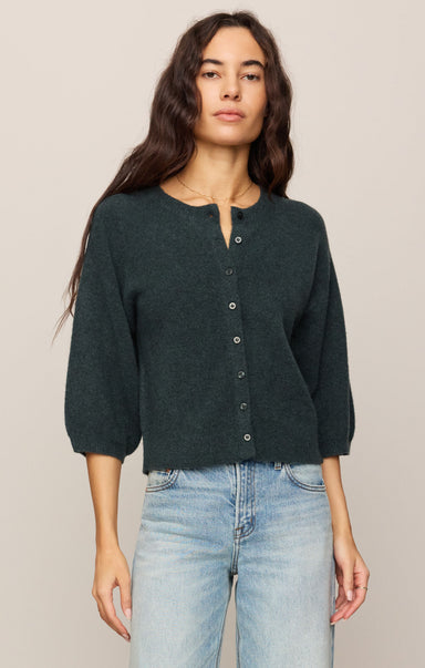Woman wearing a dark green button-up shirt and light blue jeans against a beige background