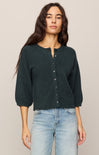 Woman wearing a dark green button-up shirt and light blue jeans against a beige background