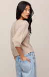 Woman wearing a beige sweater and light blue jeans against a plain background