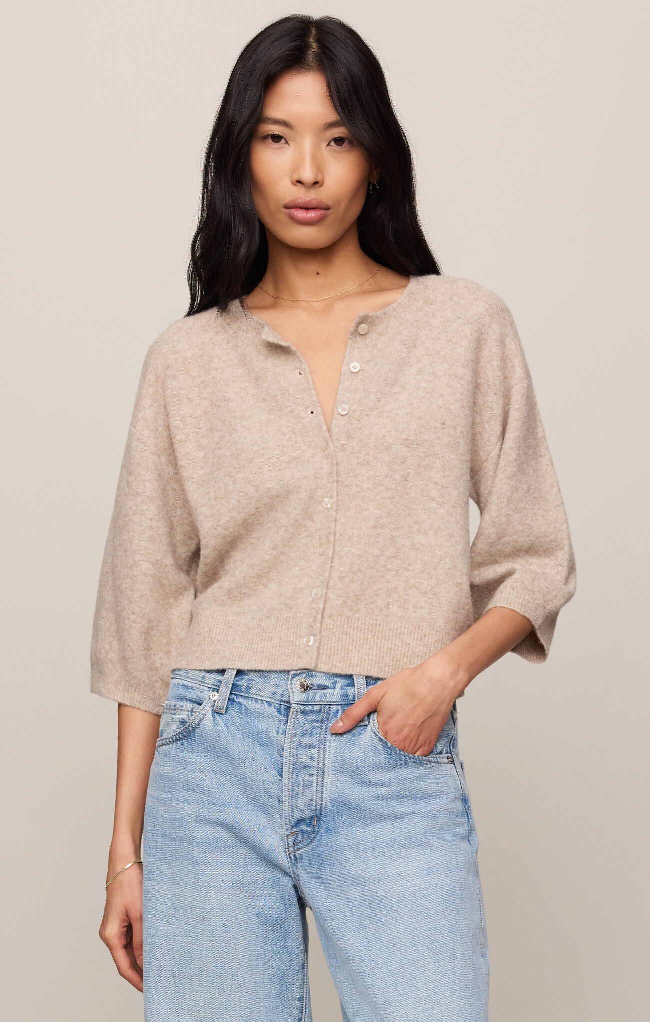 Woman wearing a beige button-up shirt and light blue jeans against a plain background