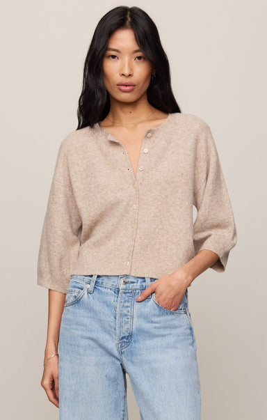 Woman wearing a beige button-up shirt and light blue jeans against a plain background