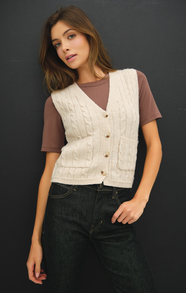 Woman wearing a cream knitted vest over a brown shirt against a black background