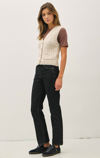 Woman wearing a cream cardigan, brown shirt, black jeans, and black shoes on a white background