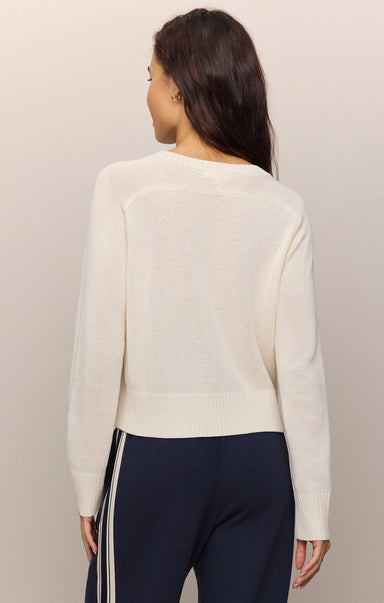 Woman wearing a cream sweater and dark pants against a plain background
