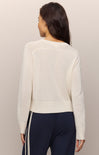 Woman wearing a cream sweater and dark pants against a plain background