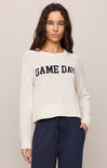 Woman wearing a white sweater with 'GAME DAY' text and navy pants on a plain background