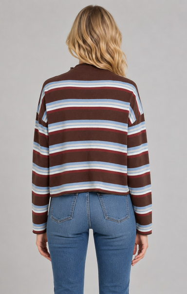 A woman viewed from the back wearing a cropped long-sleeve knit top with horizontal stripes in brown, burgundy, light blue, and white, paired with blue jeans, against a solid gray studio background.