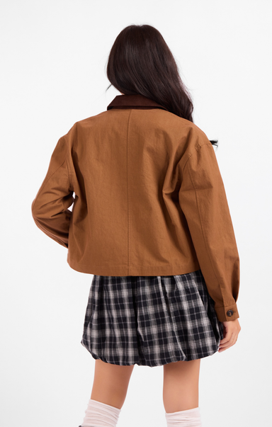 Person wearing a brown jacket and plaid skirt on a white background
