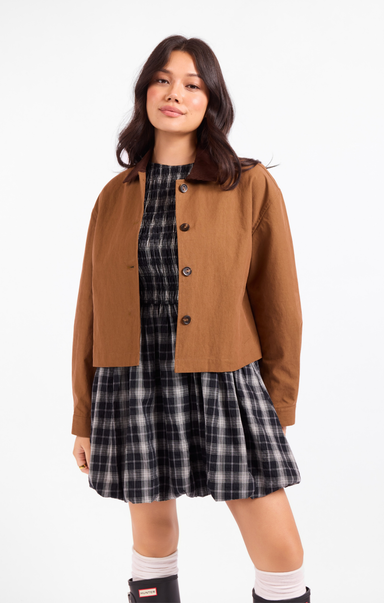 Woman wearing a brown jacket over a plaid dress on a white background