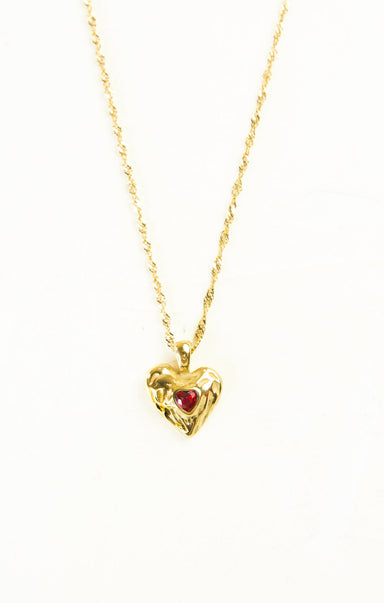 Gold heart-shaped necklace with a red gemstone on a white background