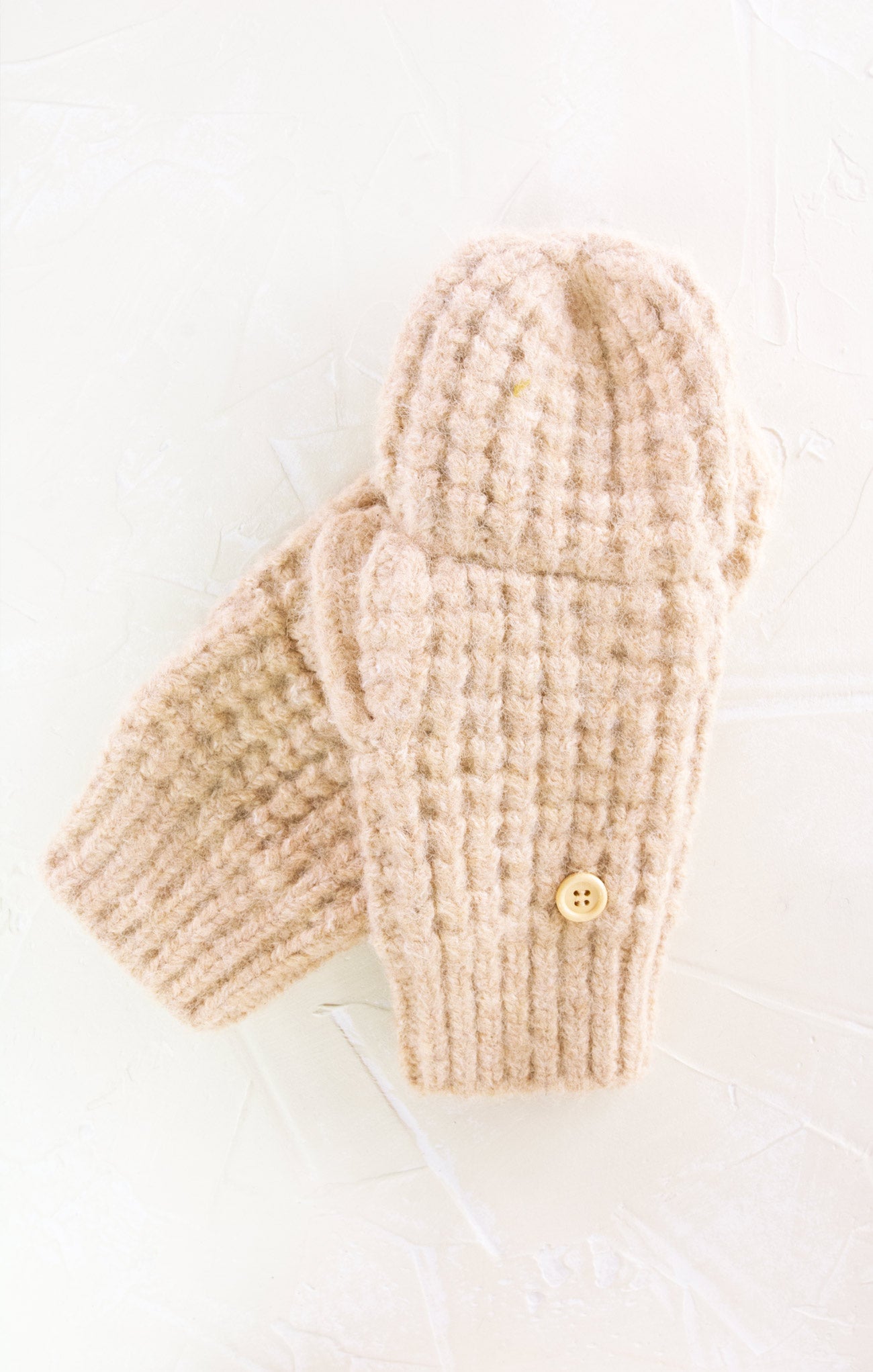 Pair of beige knitted mittens with a button on a white background